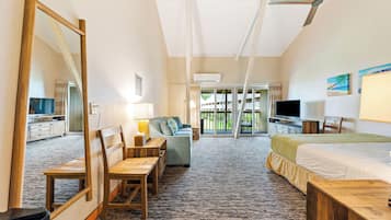 Habitación de hotel con una cama grande, un escritorio, una silla, un sofá, un televisor y un balcón con vistas al exterior.