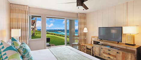 A hotel room with a bed, a TV, a desk, and a view of the ocean.