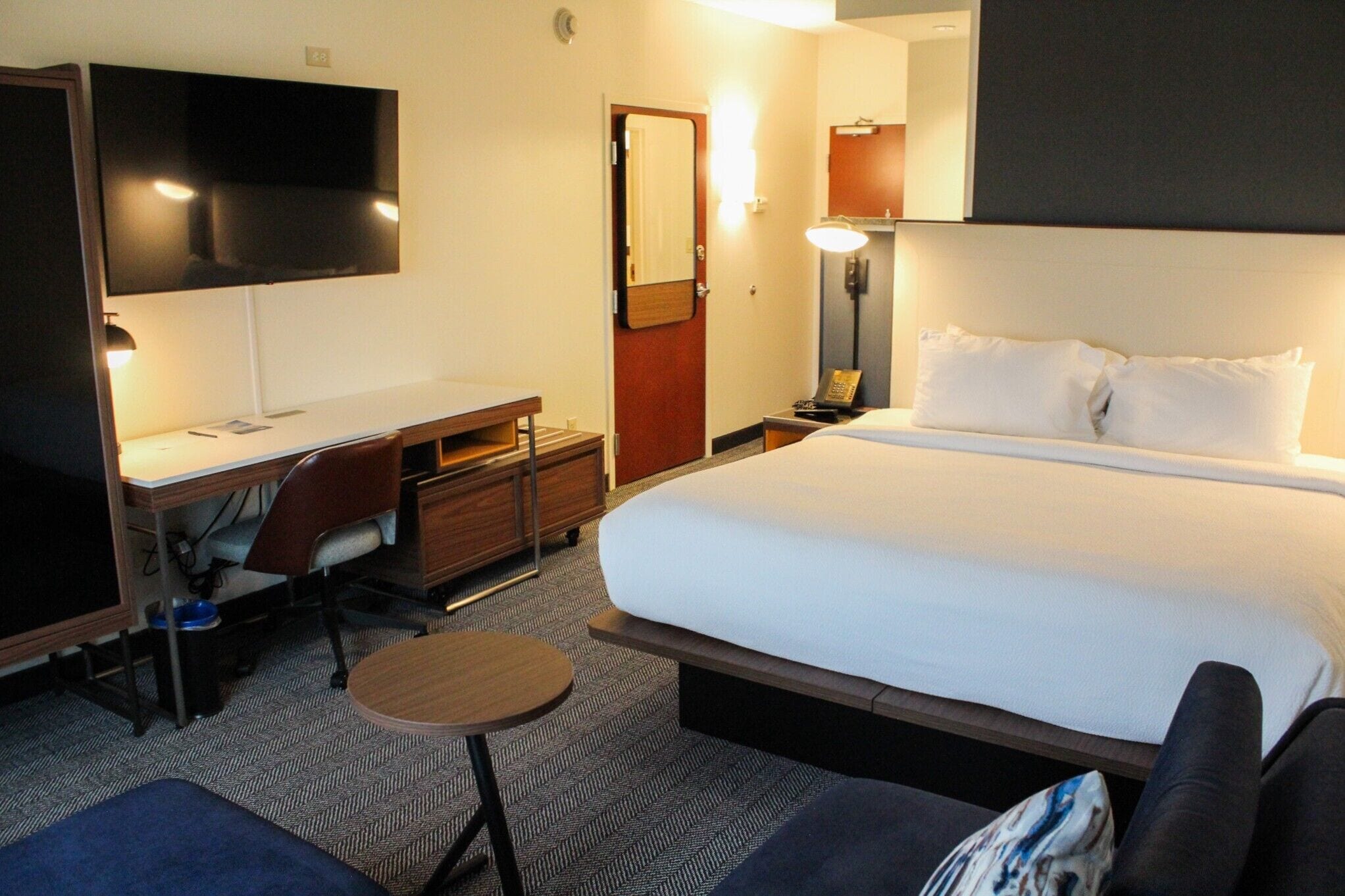 A hotel room with a bed, desk, chair, TV, and a small round table.