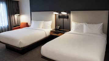 A hotel room with two beds, a nightstand with a phone, and a lamp.