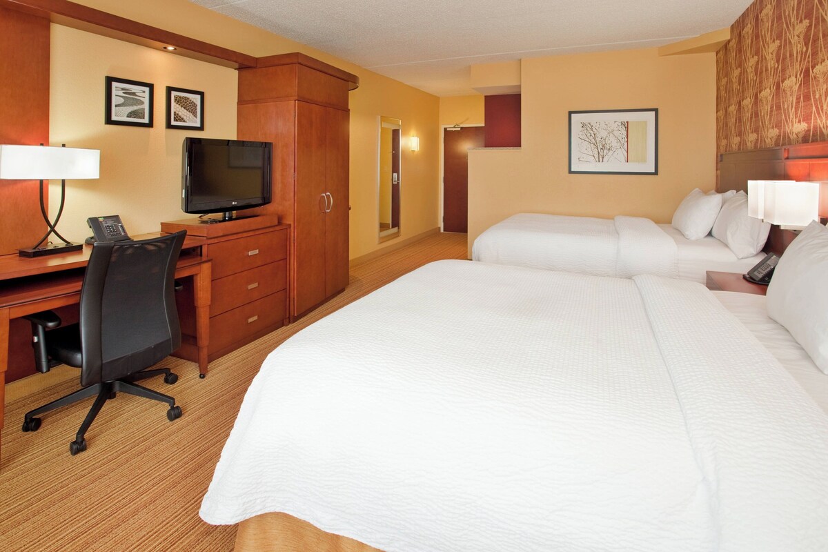 Ein Hotelzimmer mit einem großen Bett, einem Schreibtisch mit Computer und Telefon, einem Fernseher und einem Spiegel.