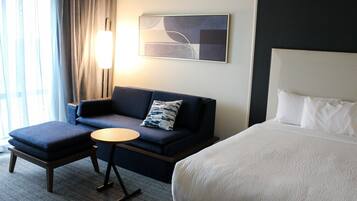 A hotel room with a bed, a sofa, a small table, and a lamp.
