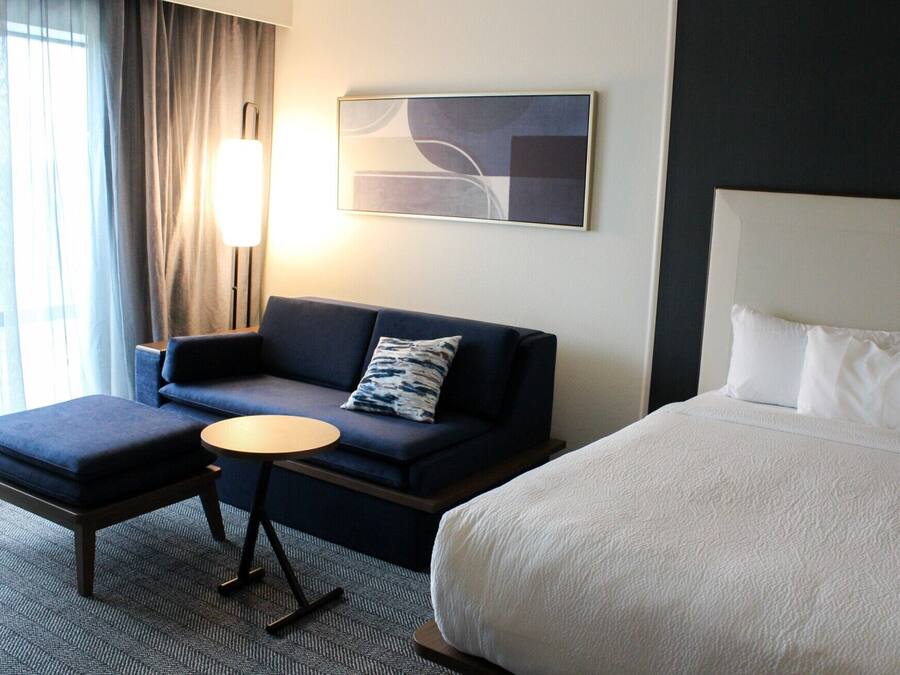 A hotel room with a bed, a sofa, a small table, and a lamp.