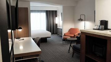 Ett hotellrum med en säng, ett skrivbord, en stol, ett litet bord, en kaffemaskin och en tv.