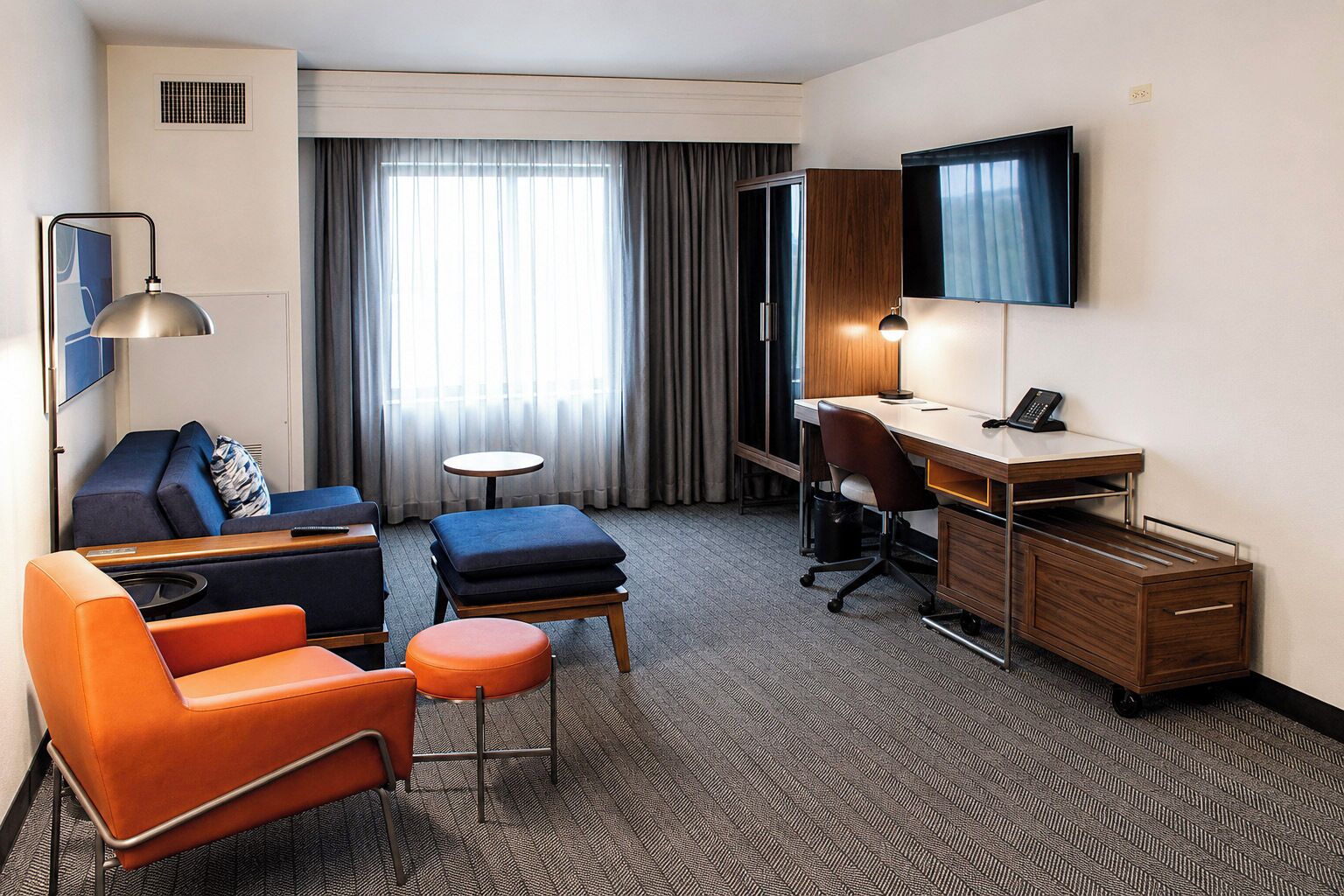 A hotel room with a desk, two chairs, a sofa, a small table, and a TV.