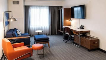A hotel room with a desk, two chairs, a sofa, a small table, and a TV.