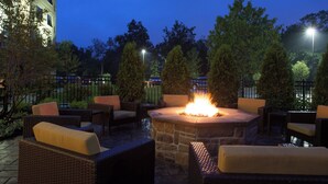 Un espace extérieur aménagé en terrasse, avec des sièges en pierre, un foyer central et une végétation luxuriante tout autour.