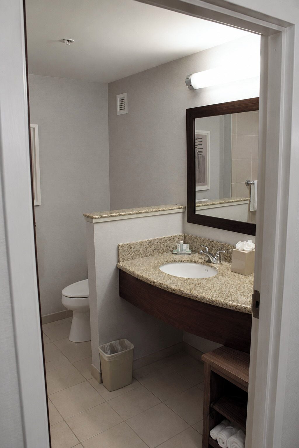 A bathroom with a sink, mirror, toilet, and a trash bin.
