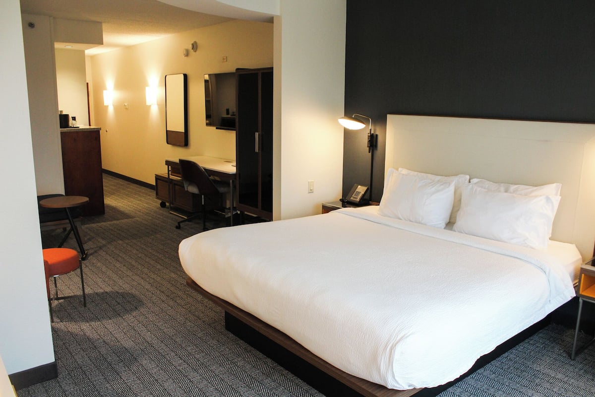 Hotellihuone, jossa on suuri sänky, työpöytä, tuoli, peili ja työpöytälamppu.