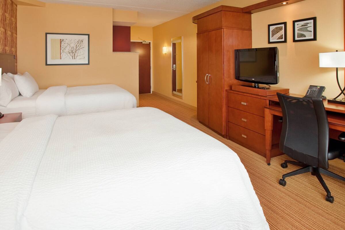 Een hotelkamer met twee bedden, een bureau met een computer, een televisie en een telefoon.