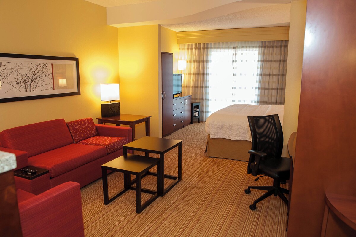 Ein Hotelzimmer mit einem roten Sofa, einem kleinen Tisch, einem Schreibtisch, einem Sessel, einem Bett und einer Kommode.