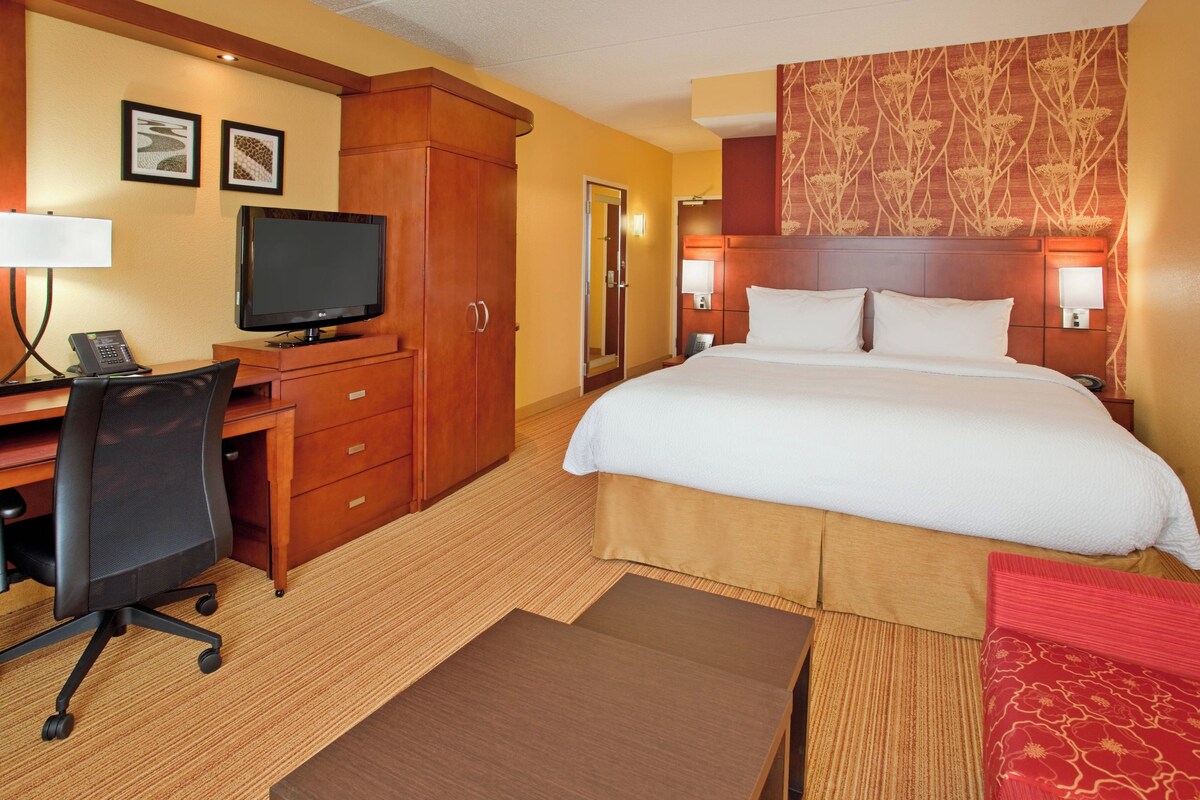 Ein Hotelzimmer mit Bett, Schreibtisch, Stuhl, Fernseher und Wandlampen.
