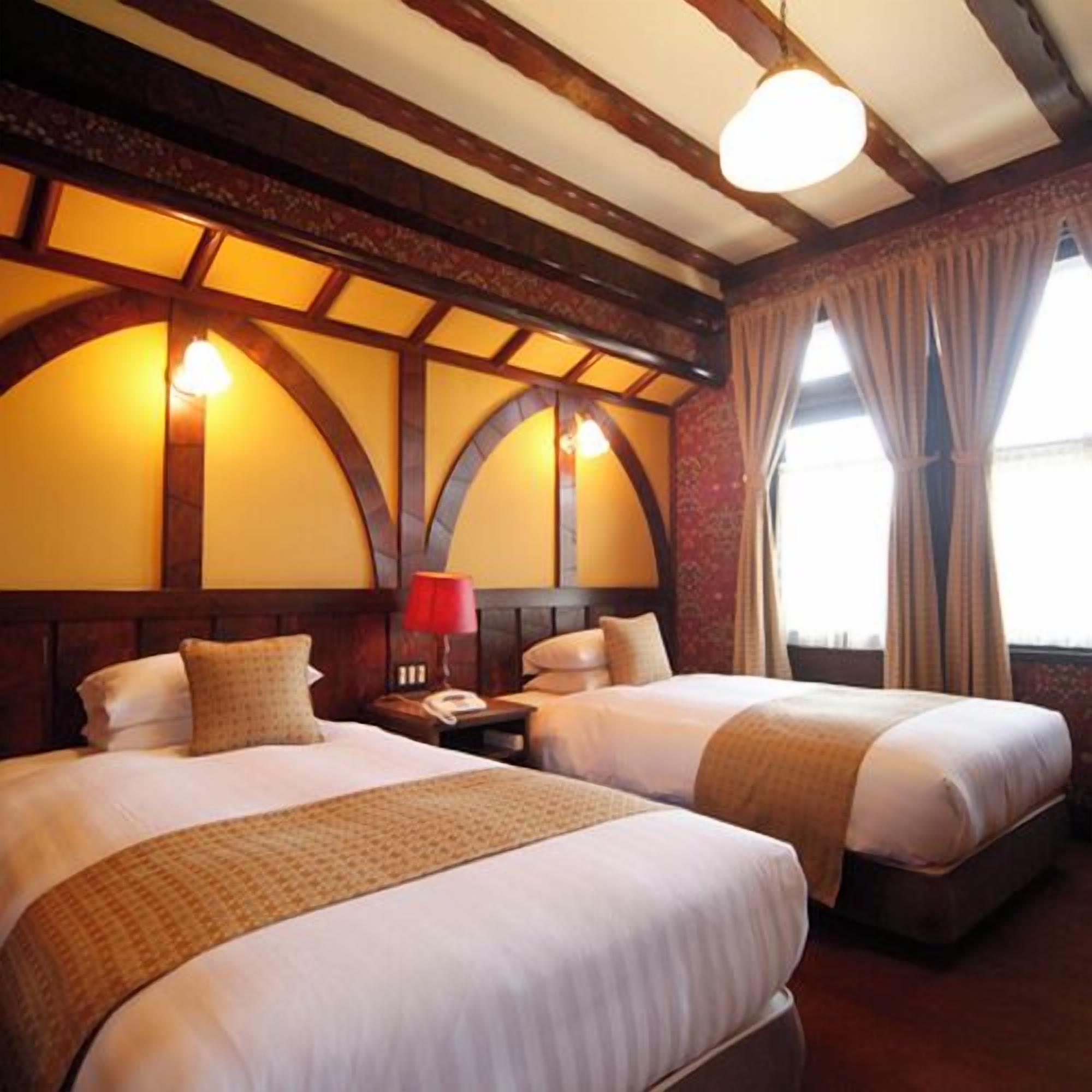 A hotel room with two beds, a wooden ceiling, and a window with curtains.