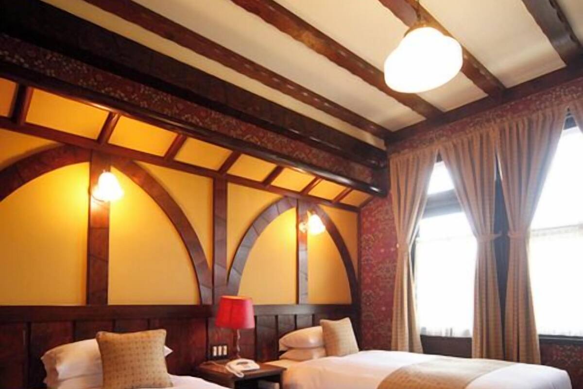 A hotel room with two beds, a wooden ceiling, and a window with curtains.