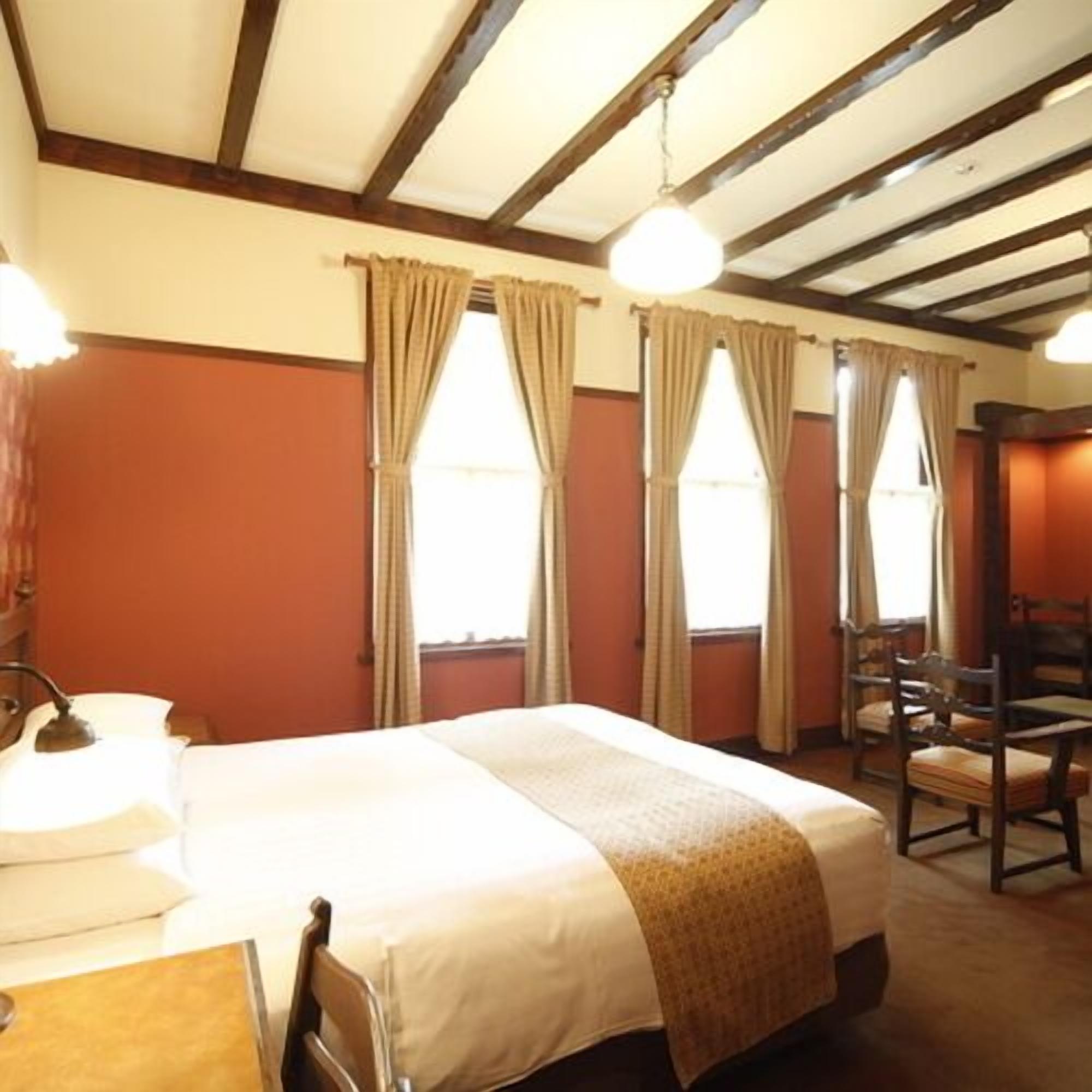 A hotel room with a bed, a desk, a chair, and a window with curtains.