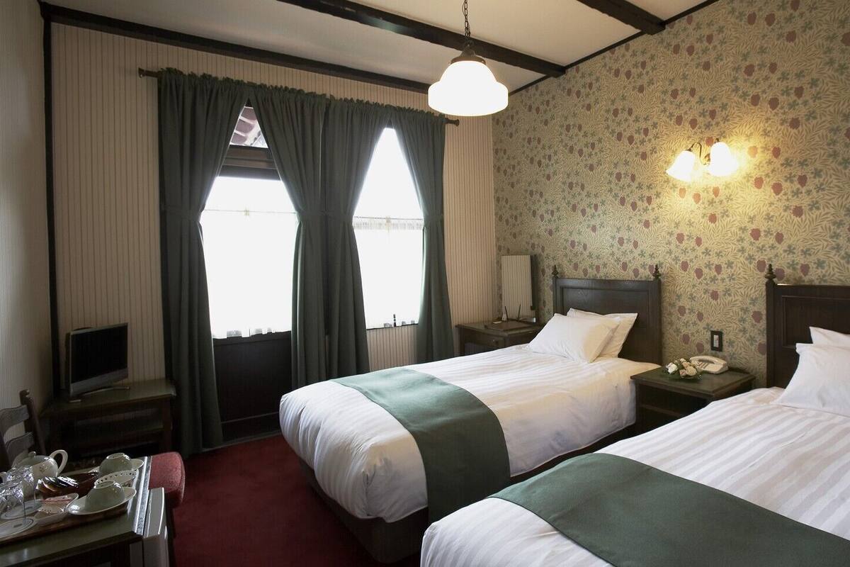 A hotel room with two beds, a television, a desk with a telephone, and a window with curtains.
