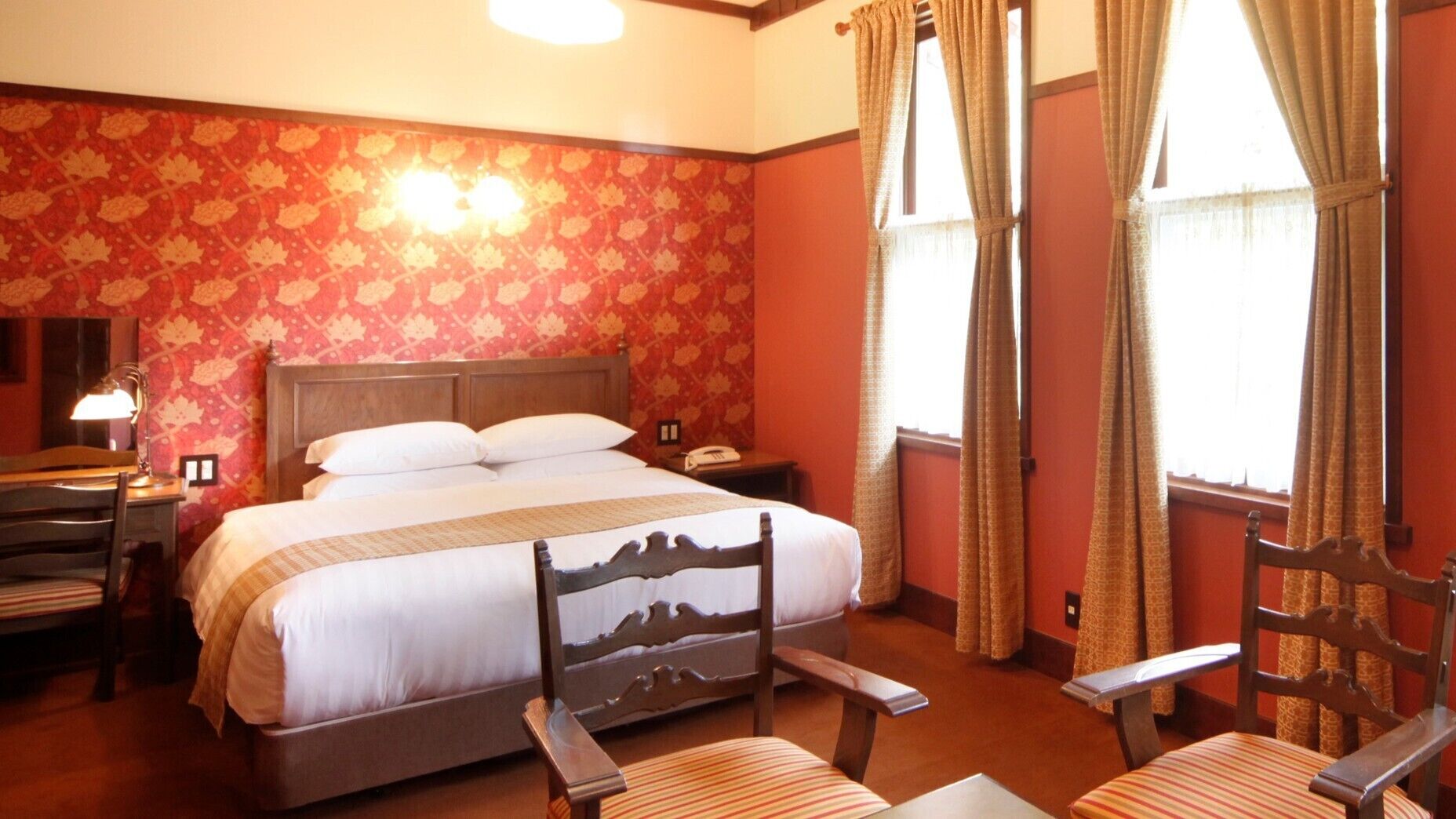 A hotel room with a bed, two bedside tables, a desk, a chair, and a window with curtains.