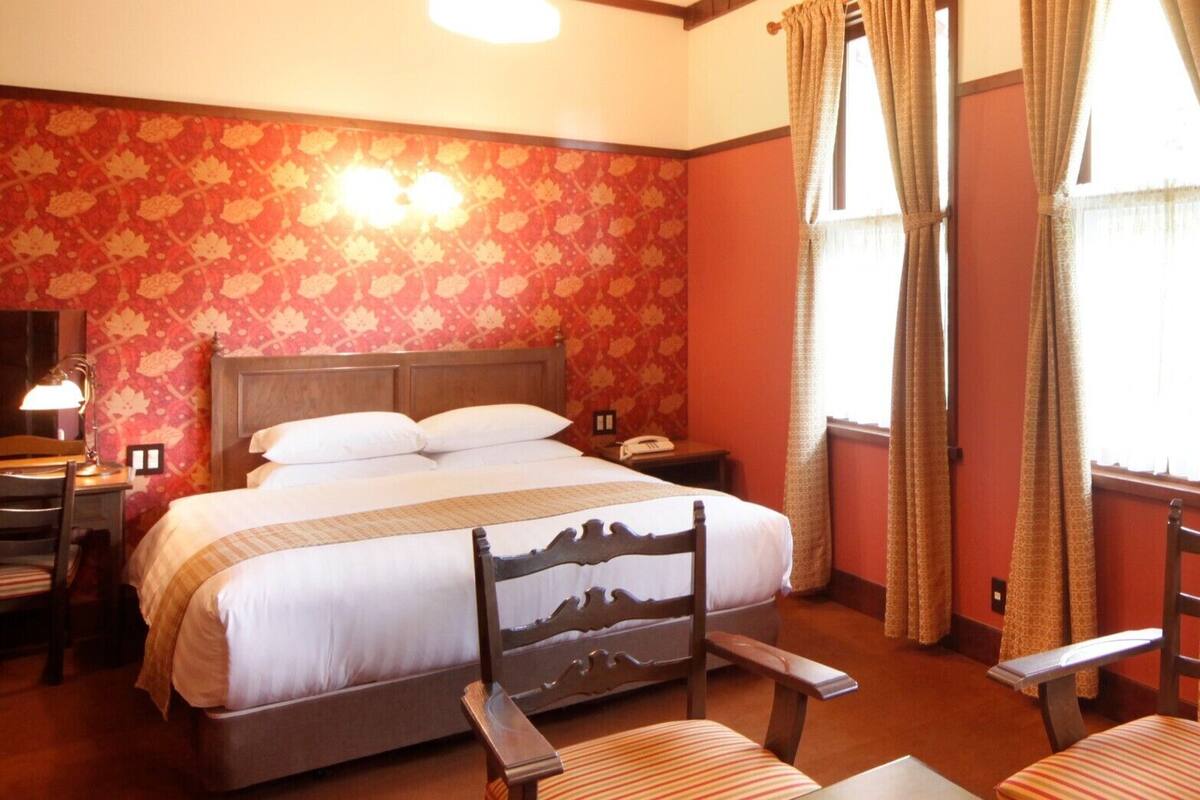 A hotel room with a bed, two bedside tables, a desk, a chair, and a window with curtains.