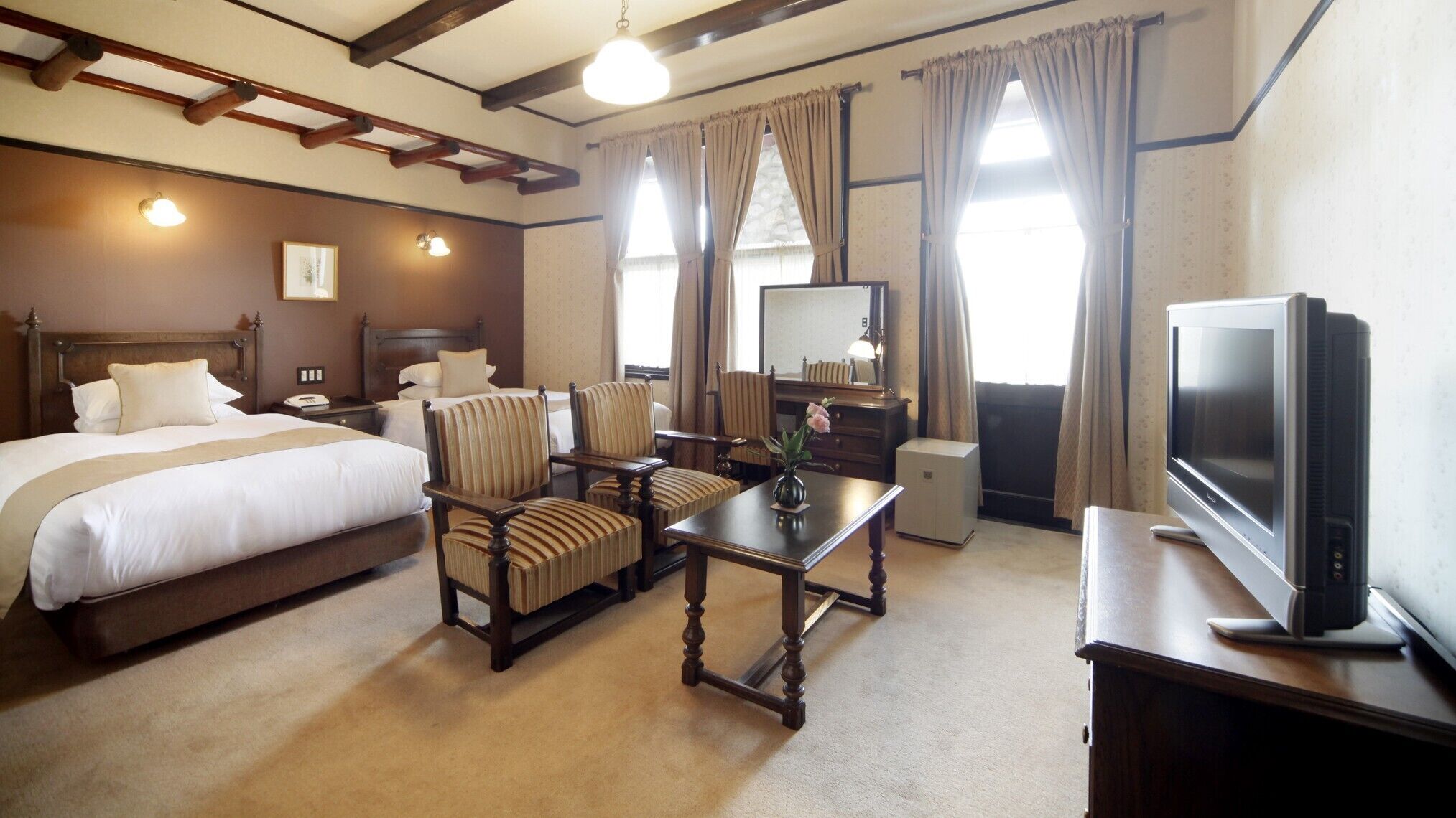 A hotel room with a bed, two armchairs, a table, a television, and a mirror.
