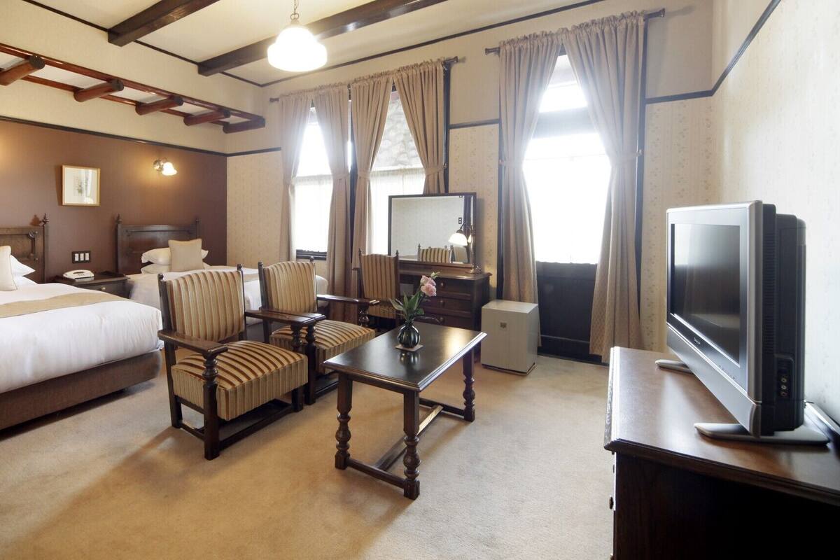 A hotel room with a bed, two armchairs, a table, a television, and a mirror.