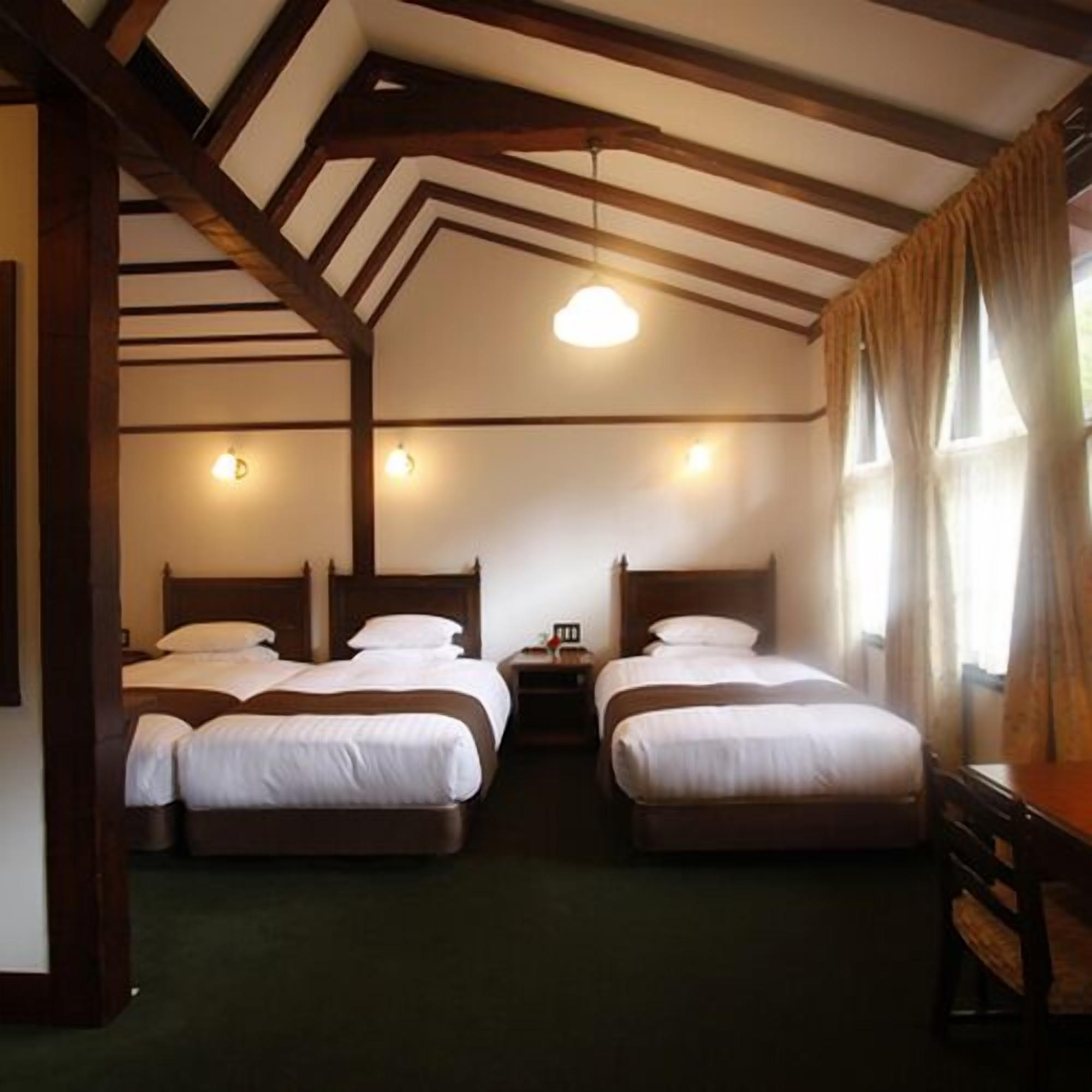 A room with two beds, wooden beams on the ceiling, and a window with curtains.