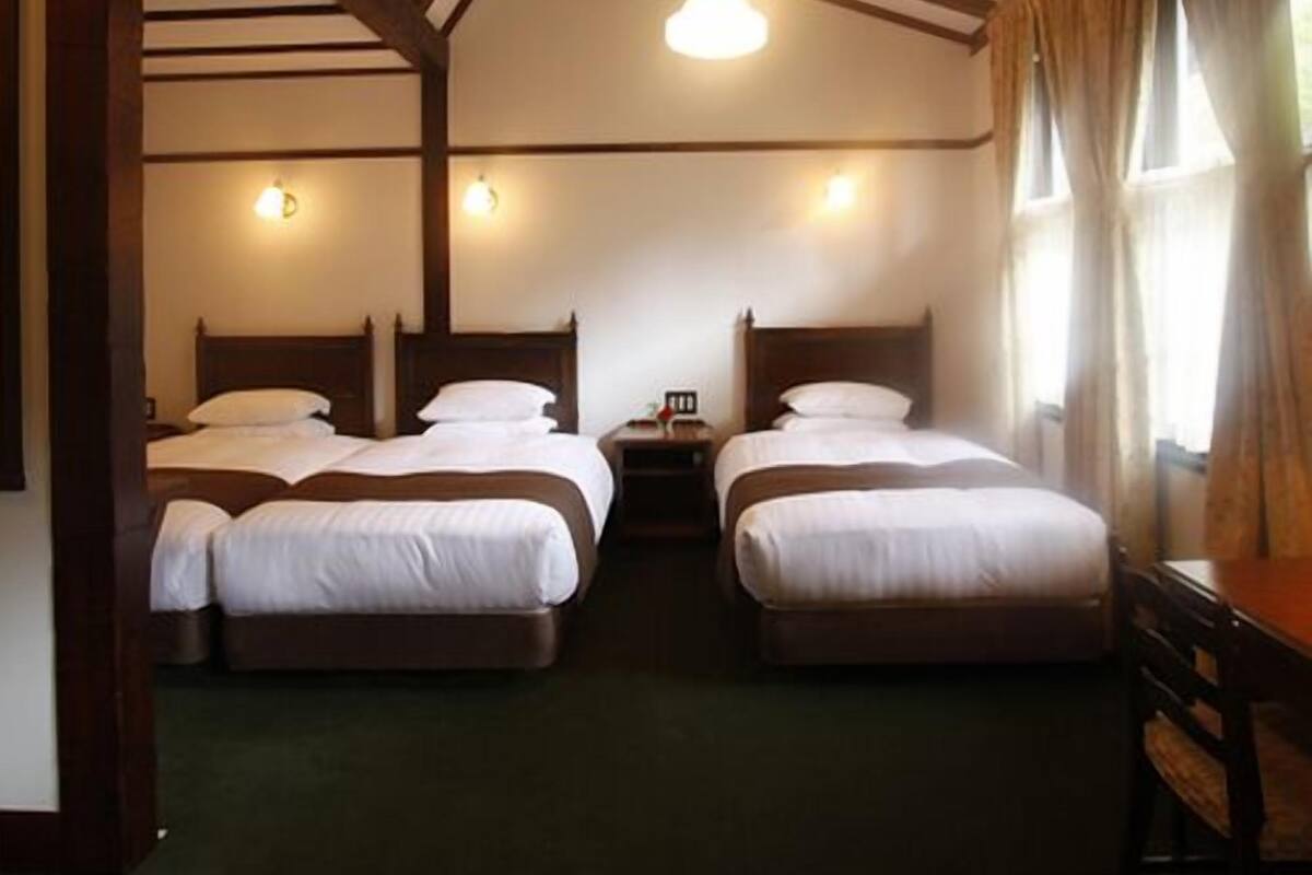 A room with two beds, wooden beams on the ceiling, and a window with curtains.
