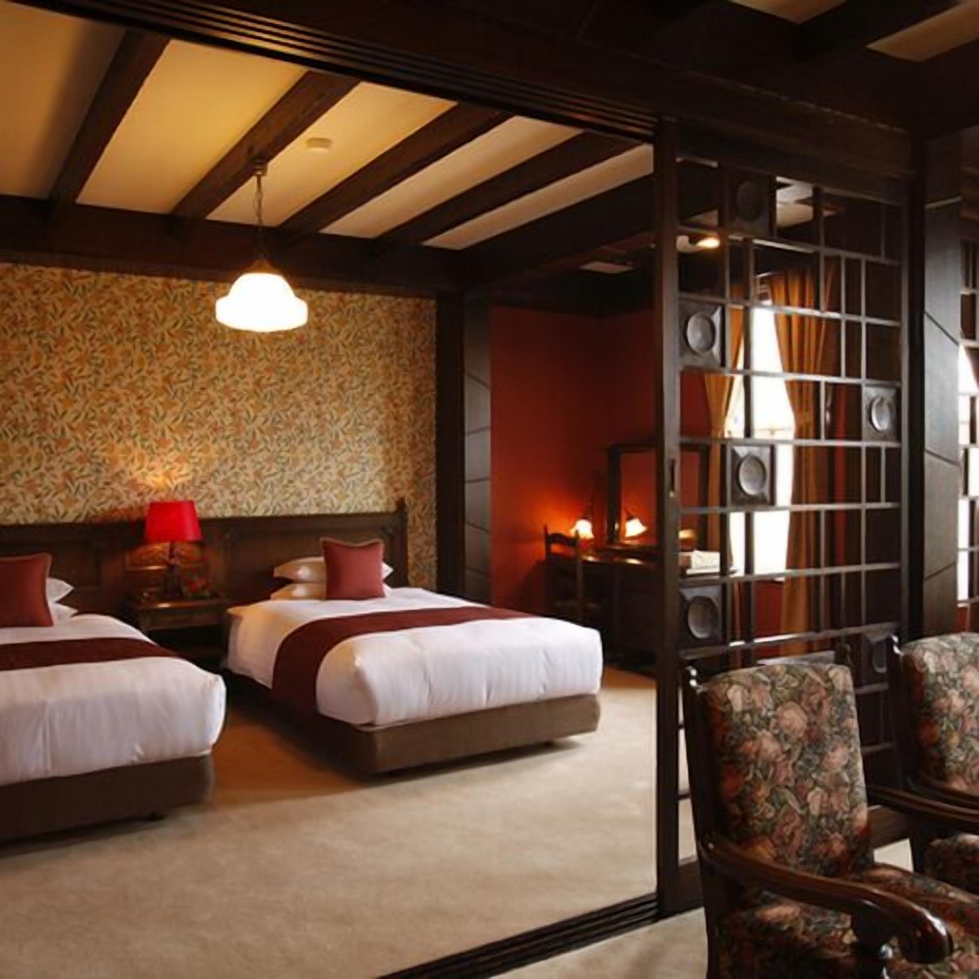A hotel room with two beds, a wooden ceiling, a patterned wall, and a seating area with a chair.