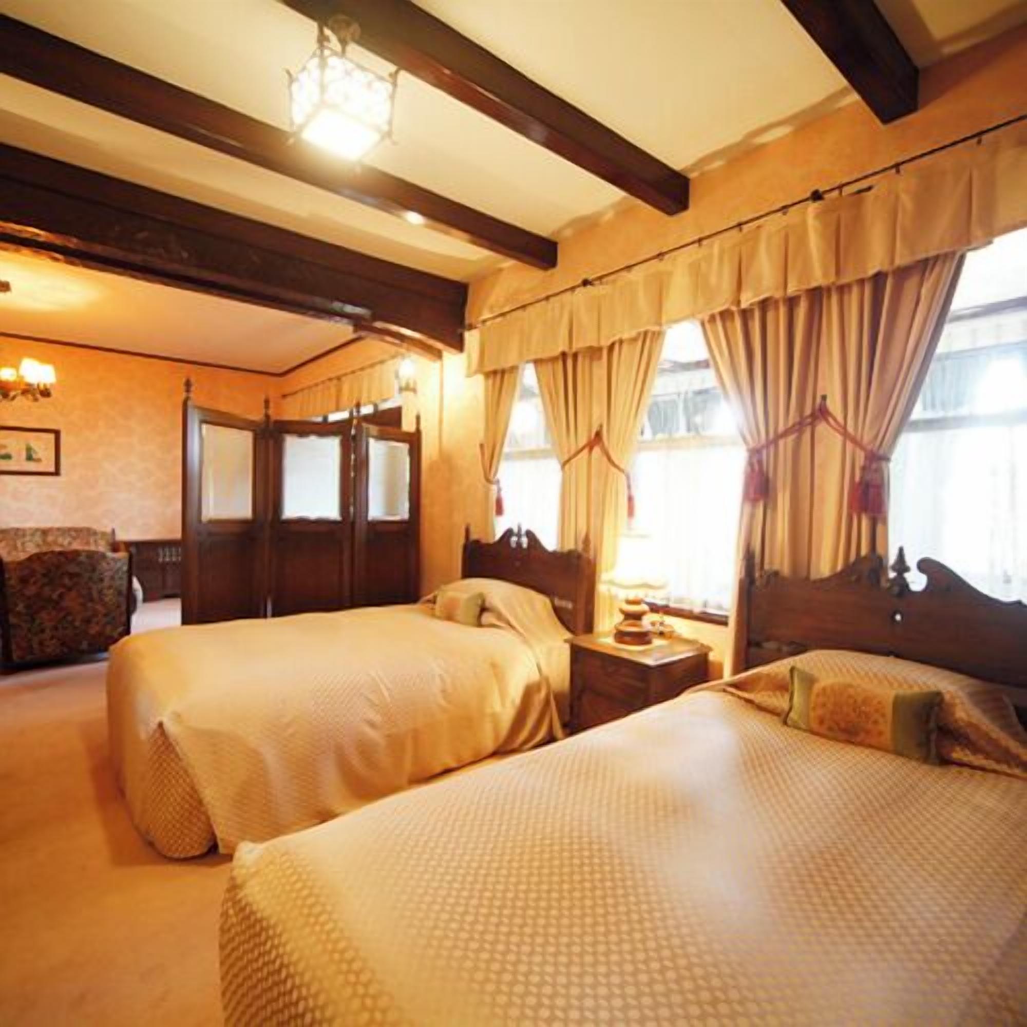A hotel room with two beds, wooden beams, a chandelier, and a window with curtains.