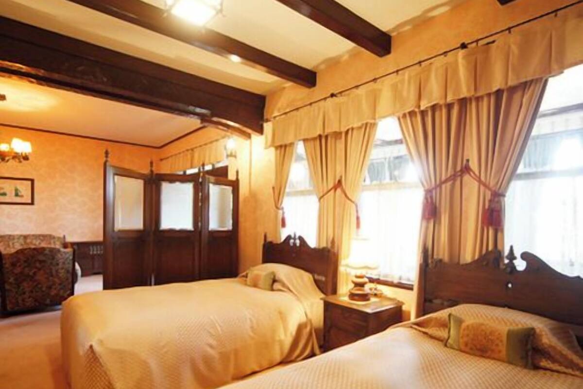 A hotel room with two beds, wooden beams, a chandelier, and a window with curtains.