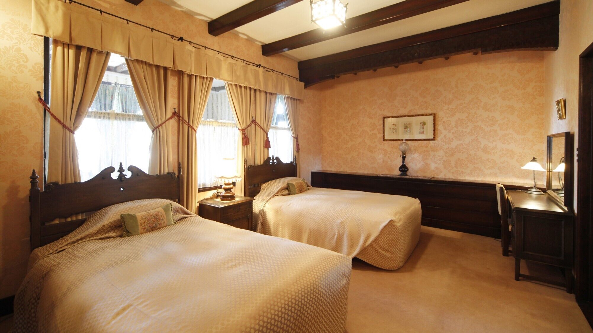 A hotel room with two beds, a nightstand, a desk with a lamp, and a framed picture on the wall.