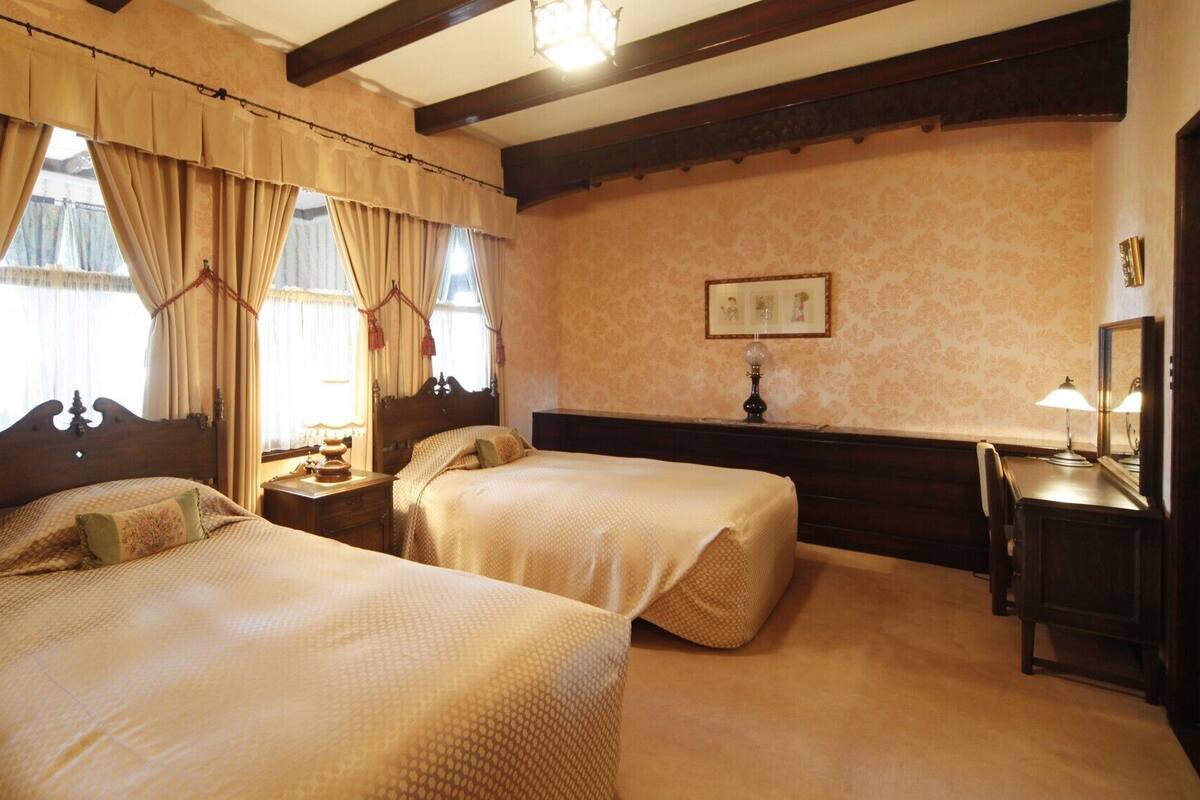 A hotel room with two beds, a nightstand, a desk with a lamp, and a framed picture on the wall.