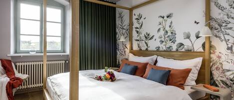 Quarto com cama de dossel, janela com persianas, radiador e papel de parede floral.