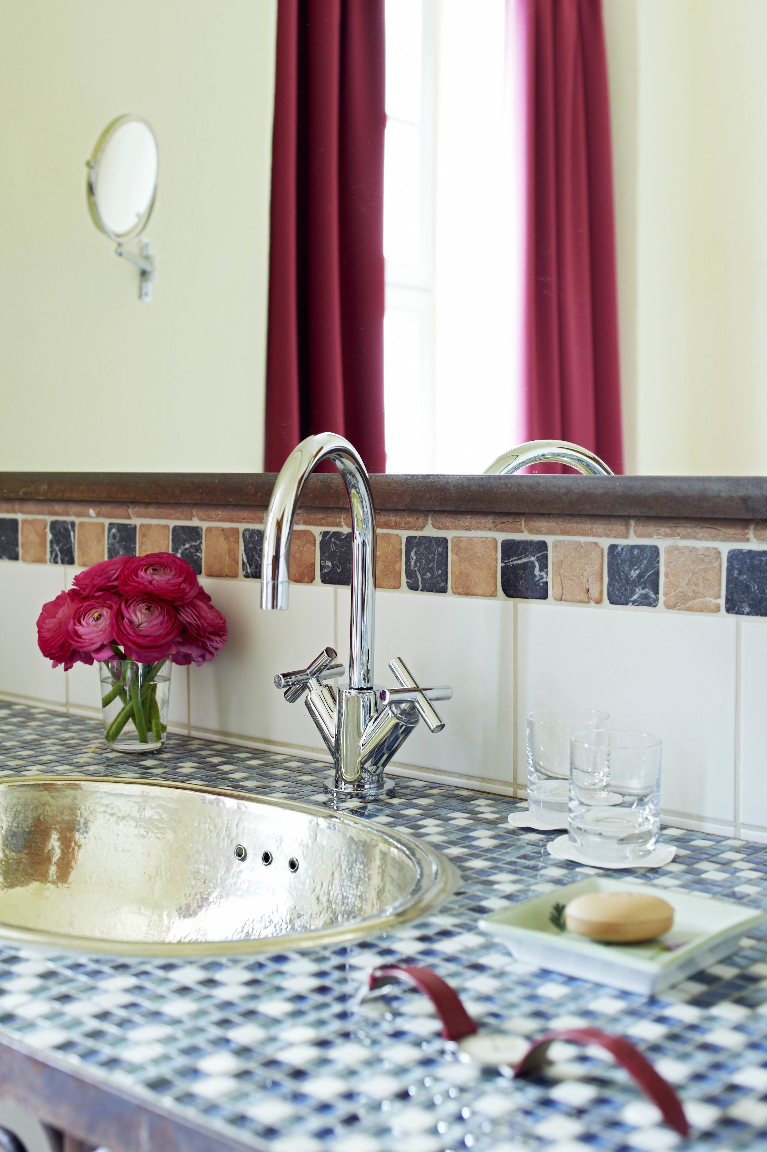 A bathroom with a sink, mirror, and a vase of flowers.