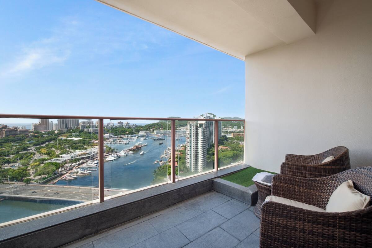Ein Balkon mit Korbmöbeln, Blick auf einen Yachthafen und hohe Gebäude.