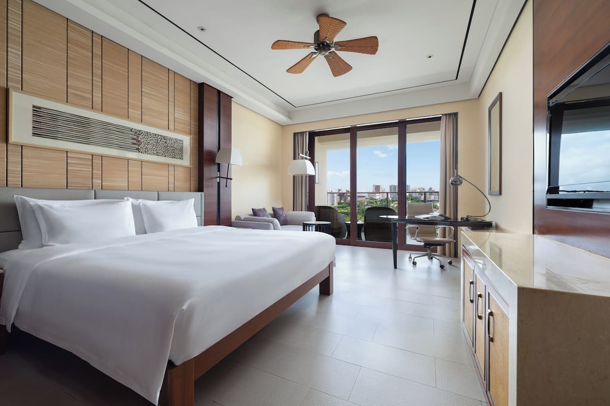 Una habitación de hotel moderna con una cama grande, un escritorio y vistas de la ciudad a través de amplios ventanales.