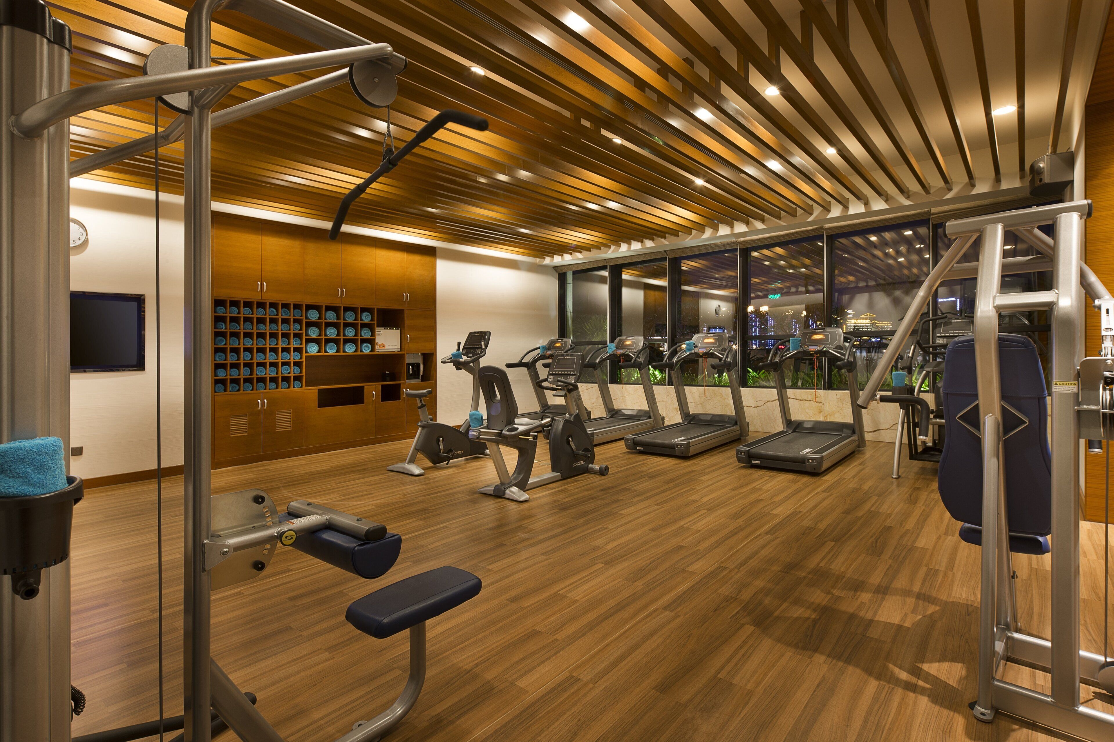 Un gimnasio con equipamiento de ejercicio, suelo de madera y amplias ventanas con vistas a la ciudad.