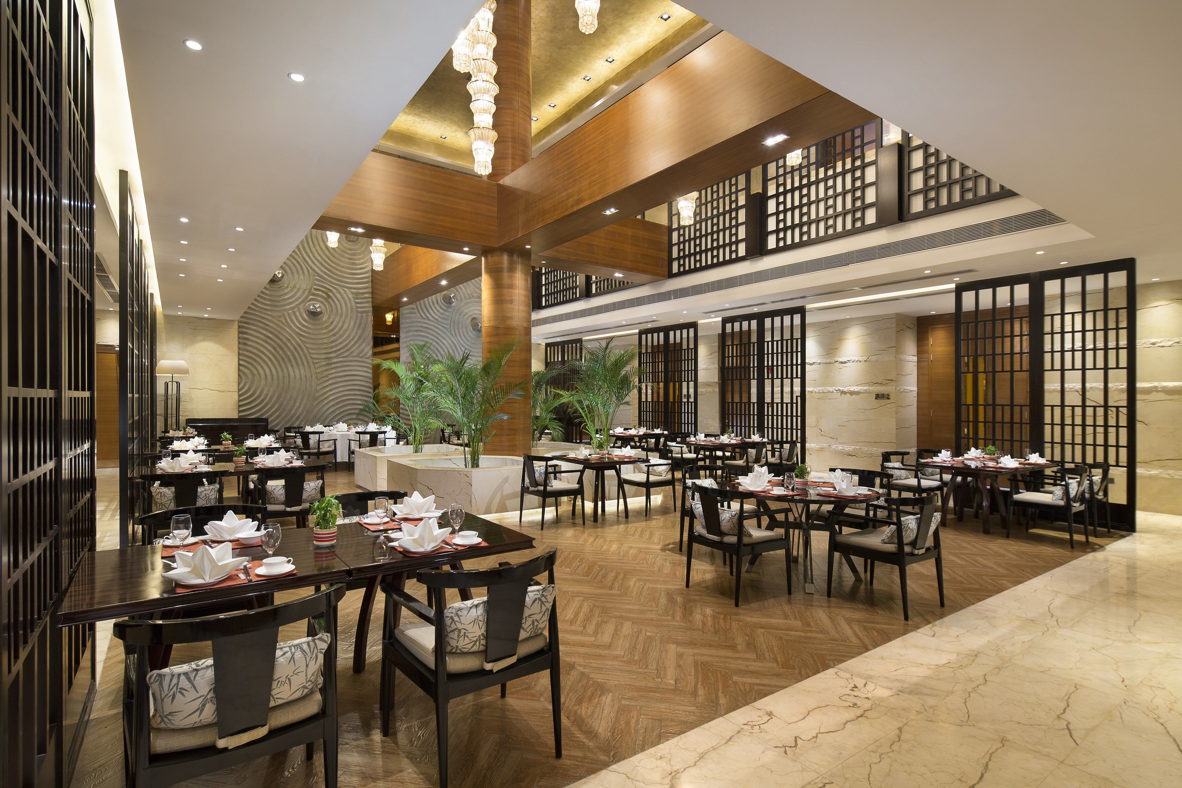 A spacious dining area with multiple tables and chairs, wooden flooring, and a high ceiling with recessed lighting.