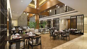 A spacious dining area with multiple tables and chairs, wooden flooring, and a high ceiling with recessed lighting.