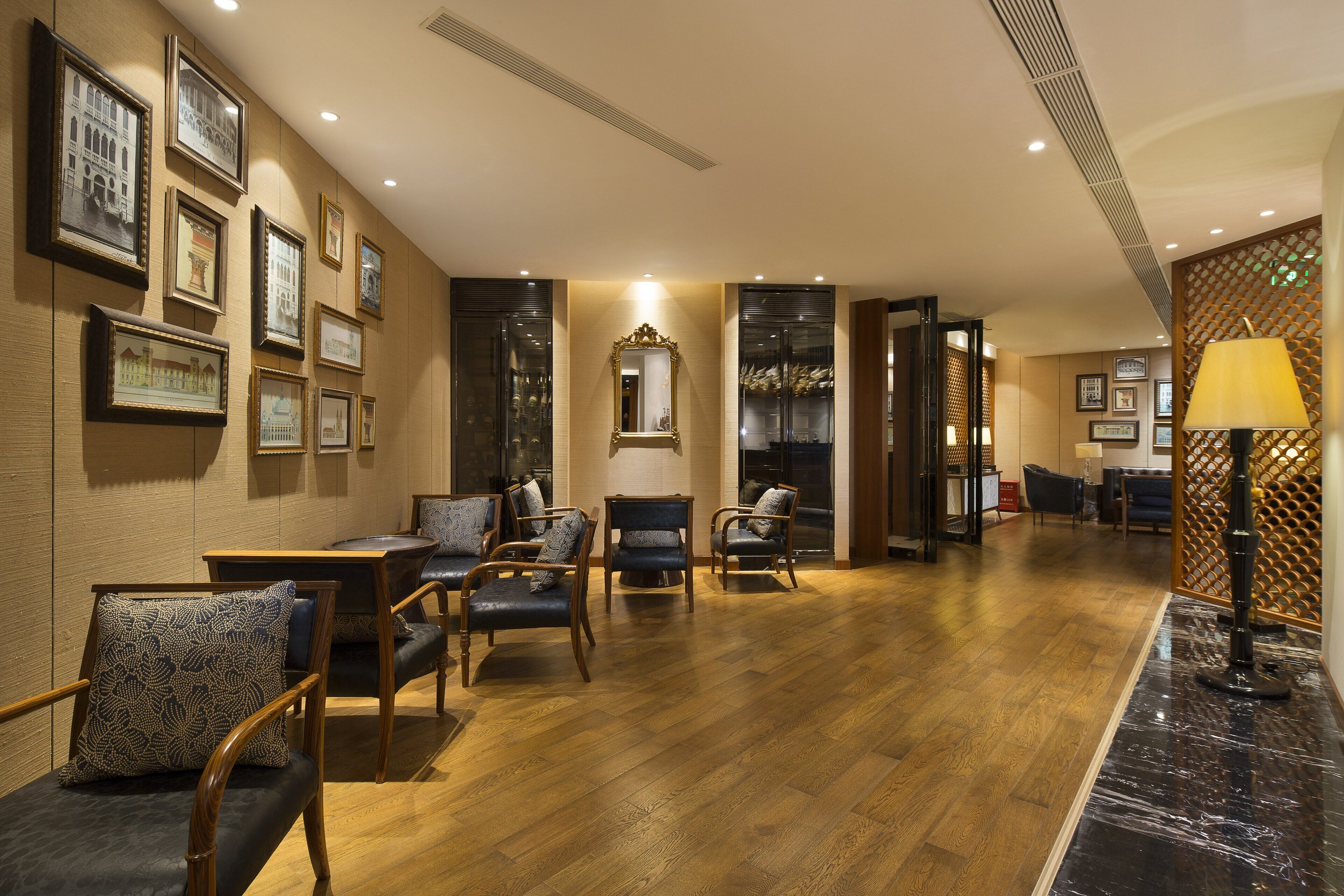 A spacious lobby with wooden flooring, several seating areas with upholstered chairs, a large mirror, and framed artwork on the walls.