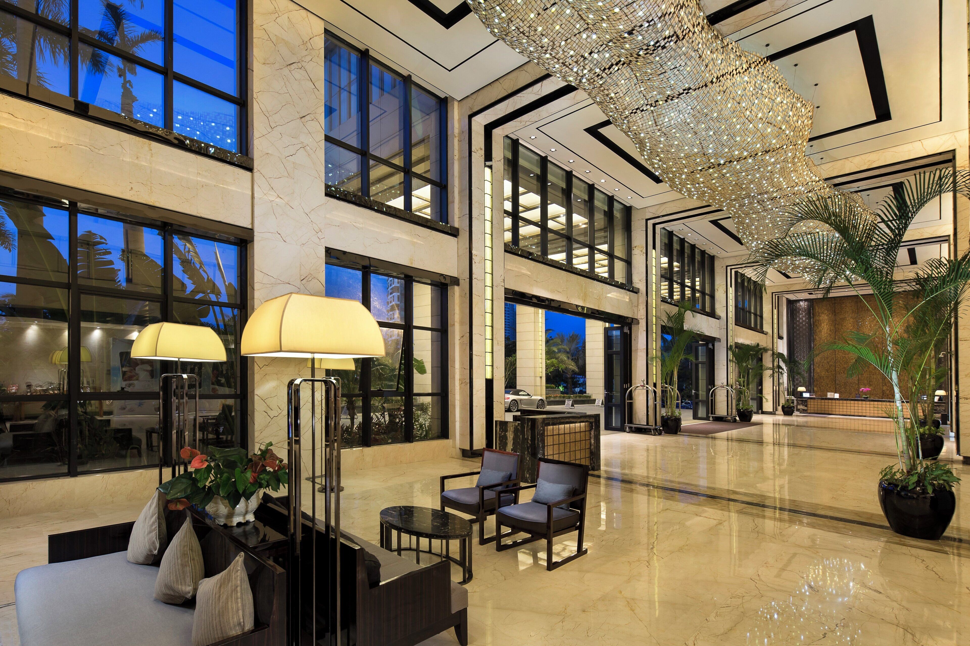 A spacious lobby with a high ceiling, large windows, and a modern chandelier.