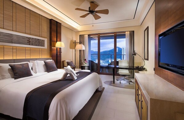 Ein Hotelzimmer mit einem großen Bett, einem Schreibtisch, einem Fernseher und einem Balkon mit Blick auf die Stadt.