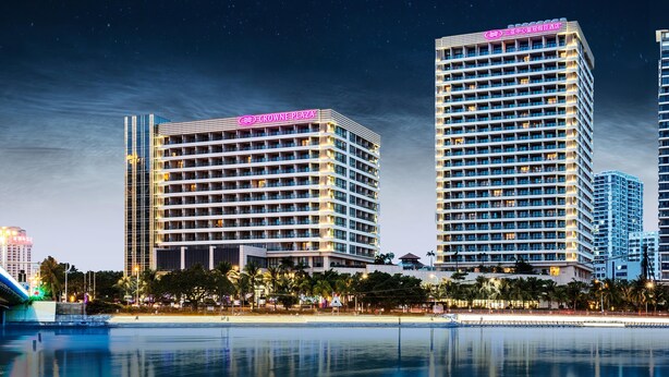 A hotel with multiple floors, a prominent sign, and a reflection in a body of water. - Crowne Plaza Sanya City Center by IHG (Sanya)