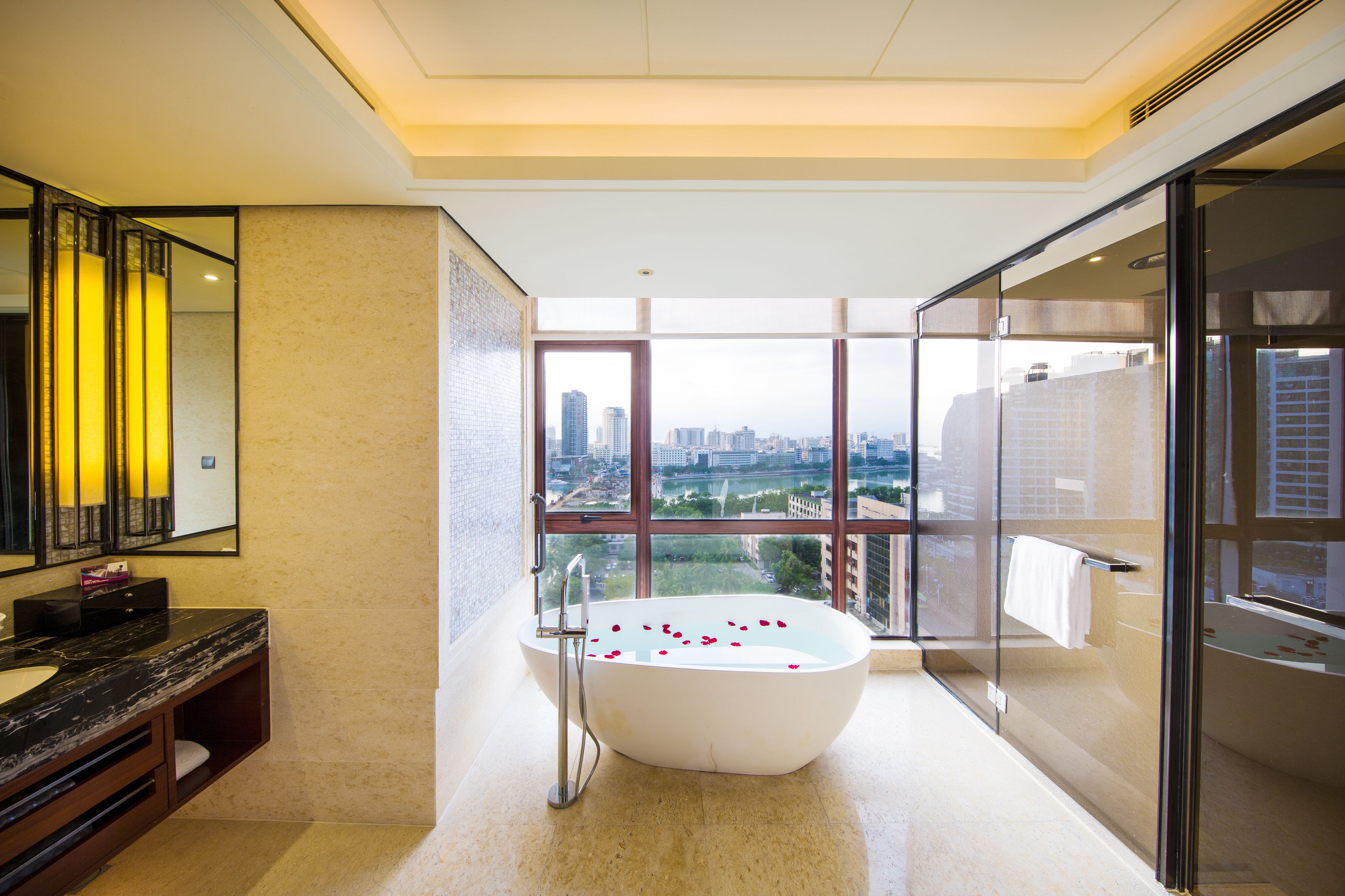 Un baño moderno con una bañera independiente, un espejo grande y vistas de la ciudad a través de amplias ventanas.