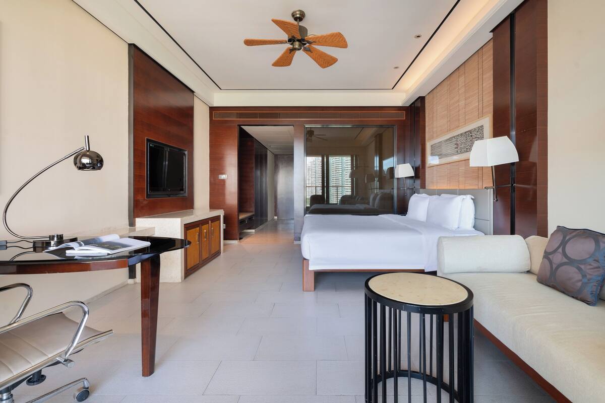 Una habitación de hotel con cama, mesita de noche, lámpara y ventilador de techo.