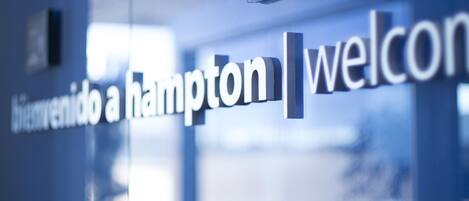 A glass wall with the words "bienvenido a Hampton" and "welcome" in English, indicating a bilingual welcome sign.
