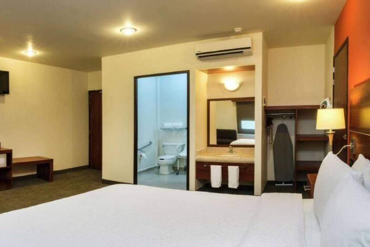 A hotel room with a bed, desk, chair, TV, and a bathroom visible through an open door.