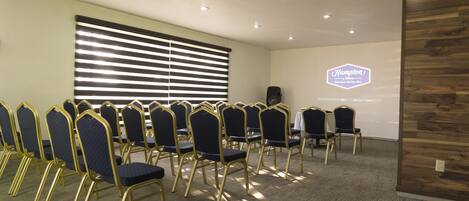 A conference room with rows of chairs, a projector screen, and a wooden accent wall.