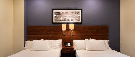 Habitación de hotel con dos camas, cabecero de madera, mesita de noche con teléfono y un cuadro en la pared.