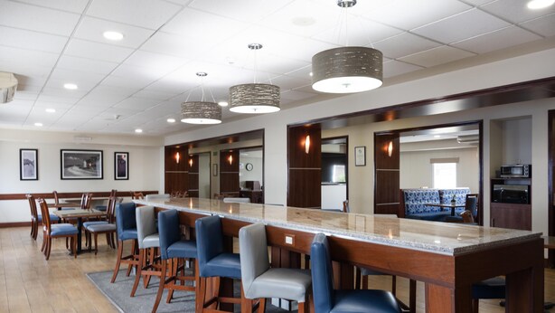 A long bar with high stools, a kitchen area, and framed pictures on the walls. - Hampton Inn by Hilton San Juan del Rio (San Juan del Río)