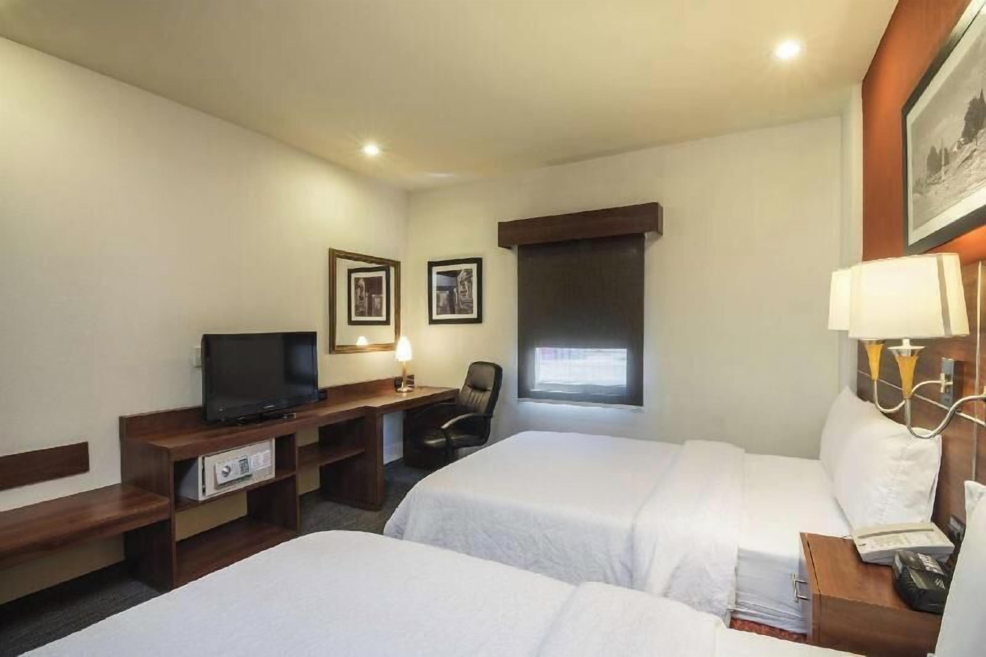 Une chambre d’hôtel avec deux lits, un bureau avec une télévision, une chaise et une fenêtre.